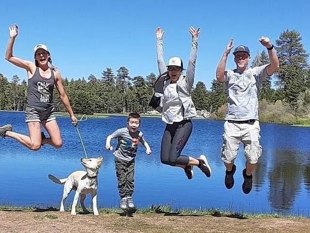 Family jumping in the air with a dog near a lake.