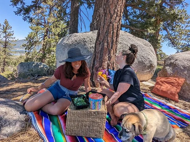 Two women having a picnic with a dog near large rocks and trees