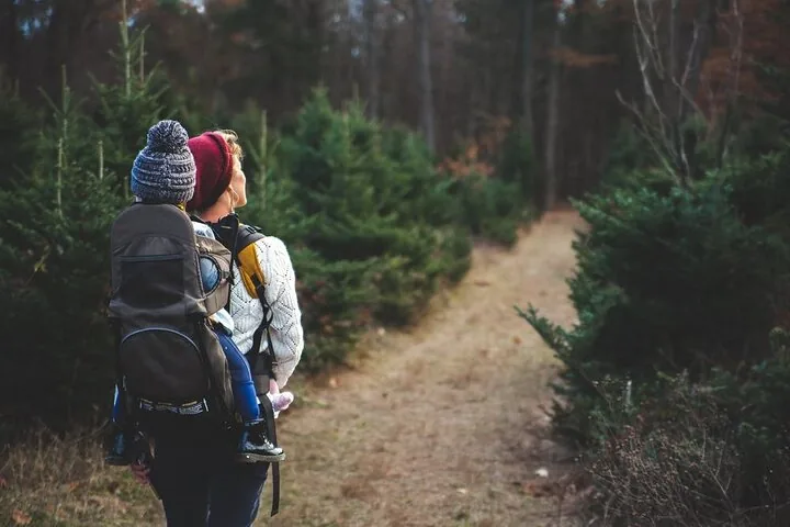 A woman carrying a small child in a backpack carrier on a trail